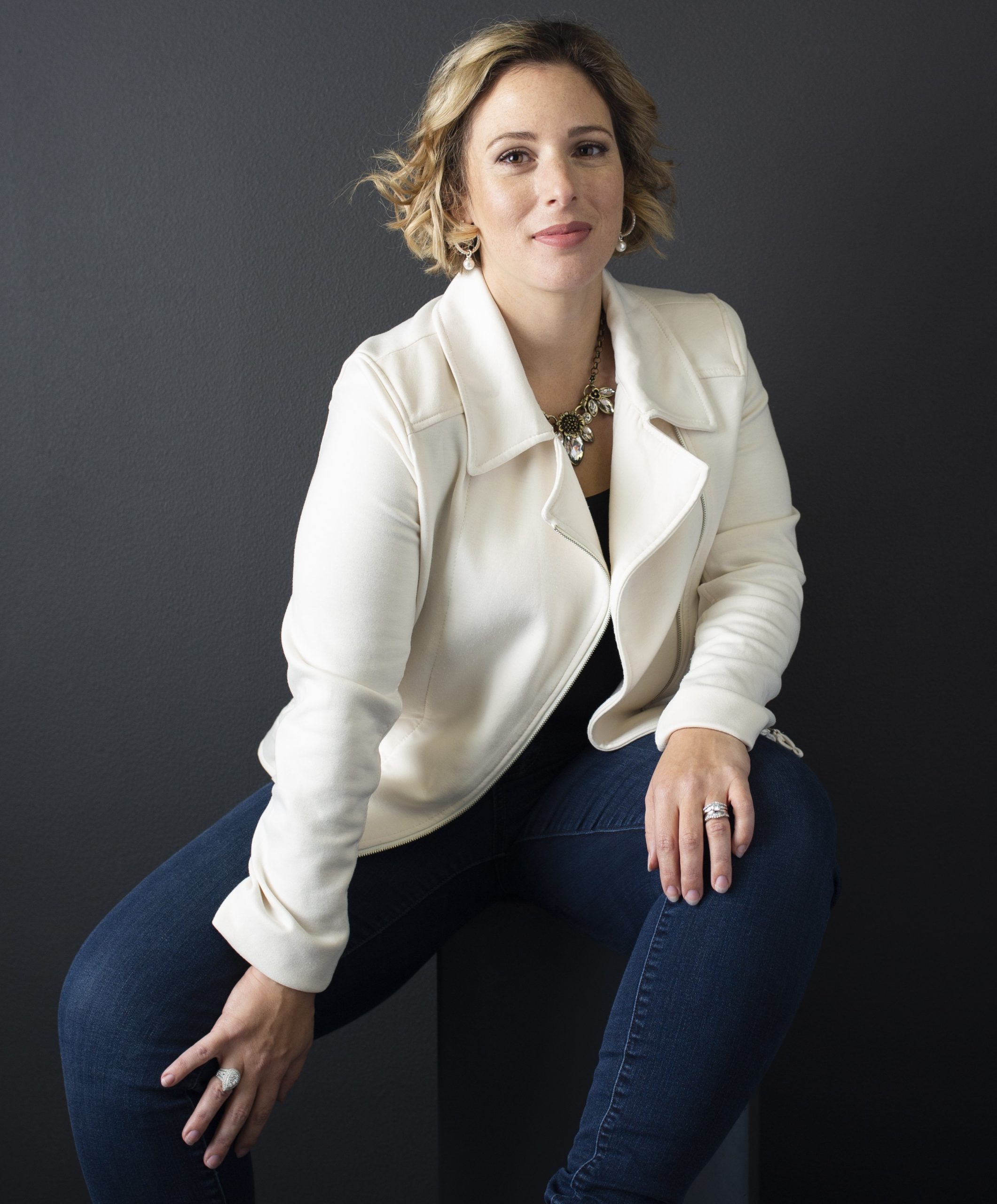 Annmarie Gustafson - Productivity Coach Annmarie Gustafson - Productivity Coach wears a white cotton motorcycle-style jacket and blue jeans while smirking at the camera.